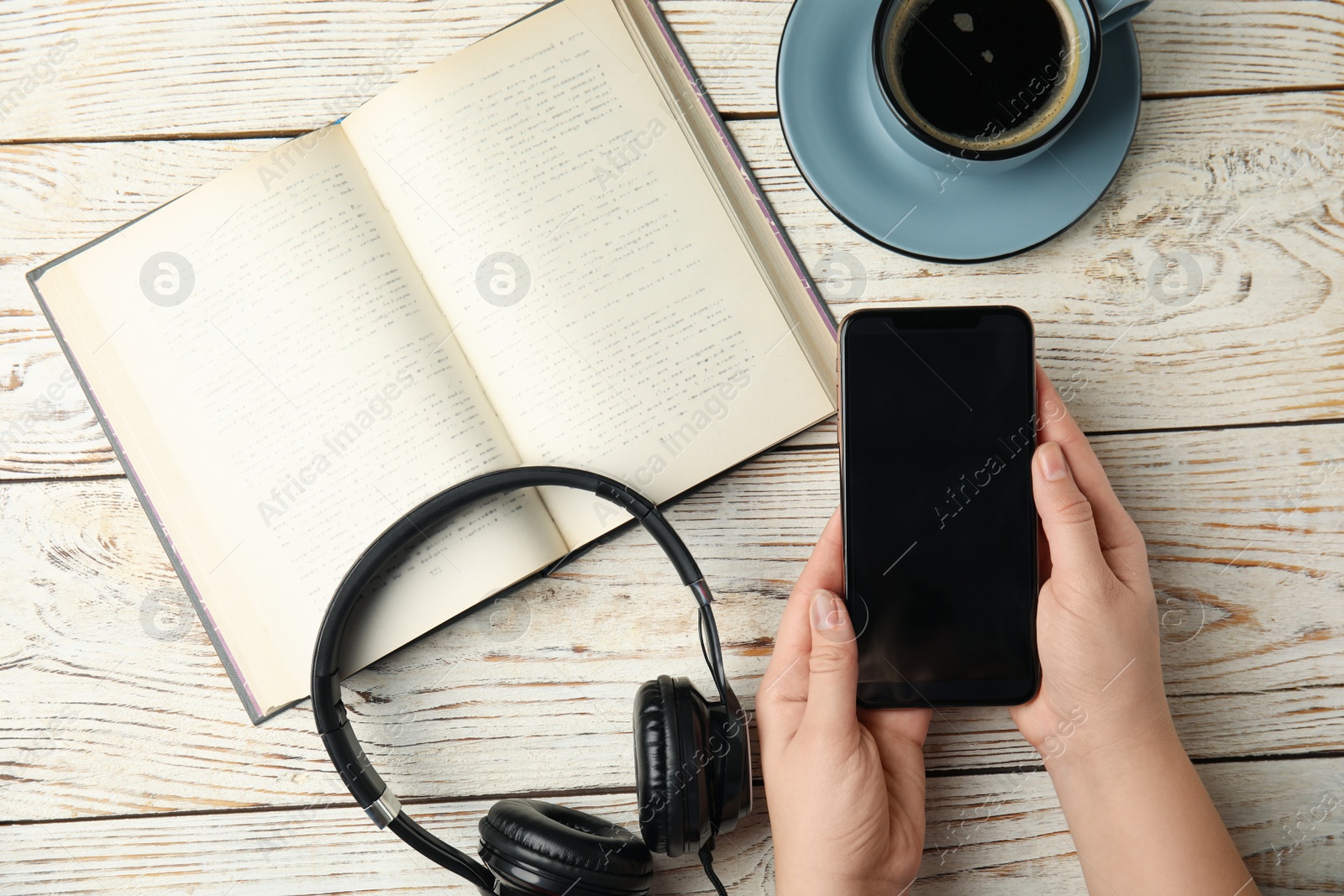 Photo of Woman holding mobile phone over white wooden table with book, top view