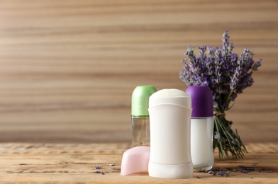 Photo of Different female deodorants and lavender flowers on wooden background, space for text