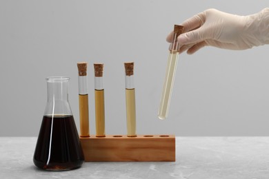 Photo of Scientist taking test tube with brown liquid from stand on light marble table, closeup