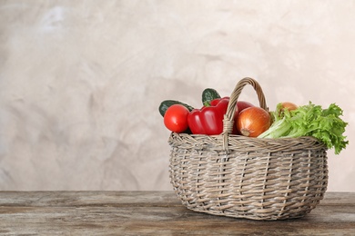 Photo of Wicker basket with ripe vegetables on wooden table. Space for text