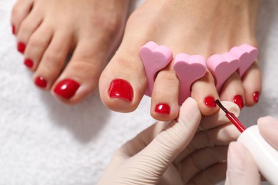 Pedicurist painting client`s toenails with red polish in beauty salon, top view