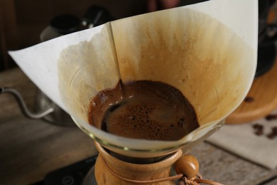 Photo of Brewing aromatic coffee in glass chemex coffeemaker with paper filter on table, closeup