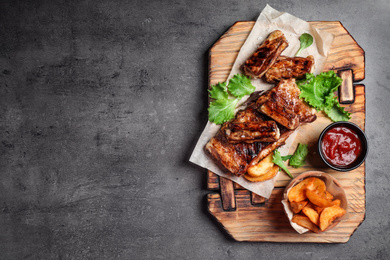 Photo of Delicious grilled ribs and garnish on grey table, top view. Space for text
