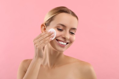 Photo of Smiling woman removing makeup with cotton pad on pink background
