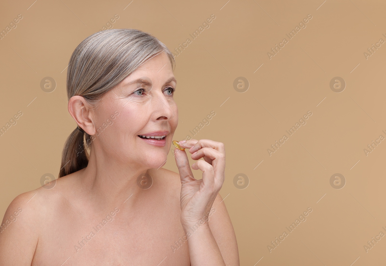 Photo of Beautiful woman taking vitamin capsule on beige background, space for text