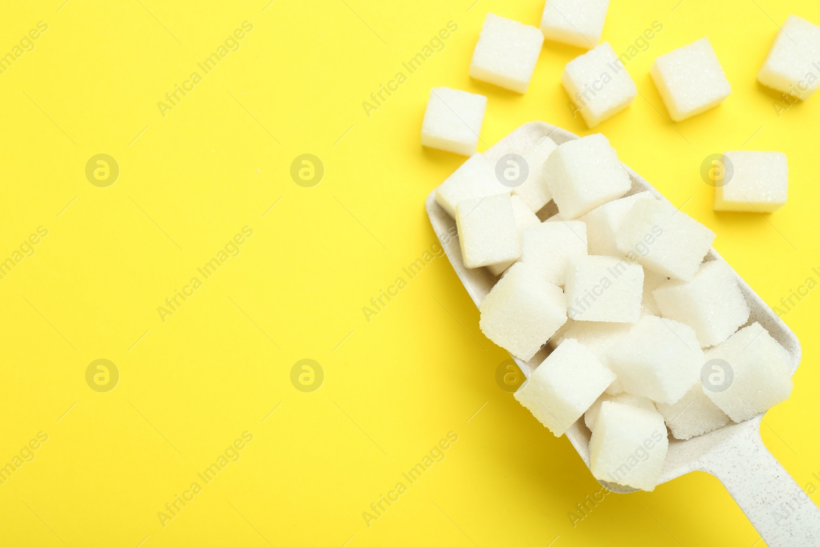 Photo of White sugar cubes and scoop on yellow background, top view. Space for text