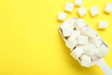 Photo of White sugar cubes and scoop on yellow background, top view. Space for text