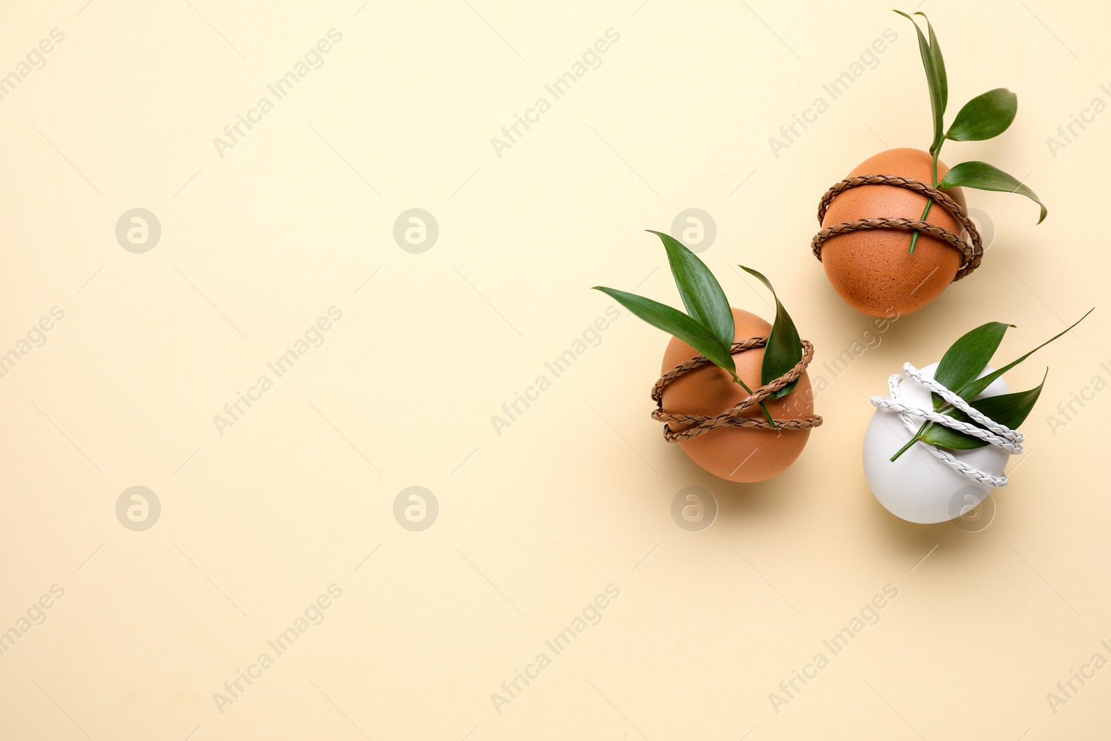 Photo of Easter eggs decorated with green leaves on beige background, top view. Space for text