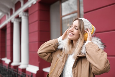 Photo of Young woman with headphones listening to music outdoors. Space for text