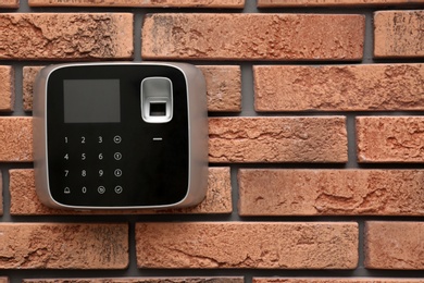 Modern alarm system with fingerprint scanner on brick wall. Space for text