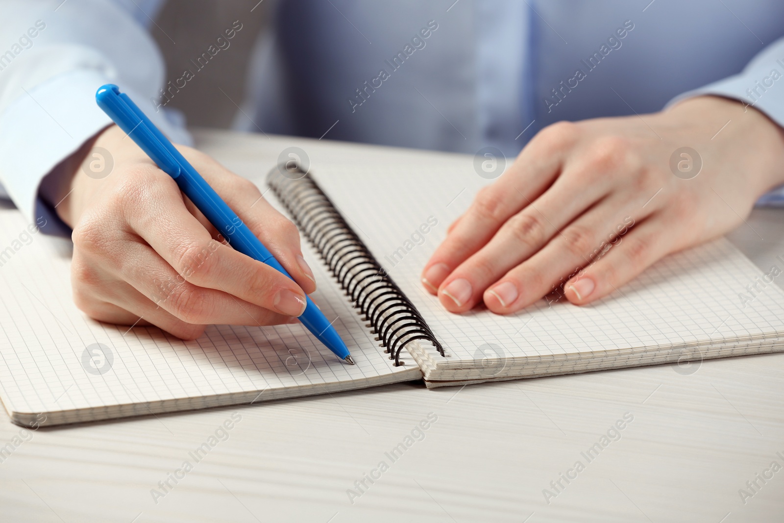 Photo of Woman writing in notebook at white wooden table, closeup