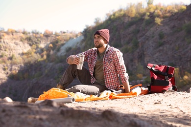 Male camper with thermos sitting on sleeping bag in wilderness