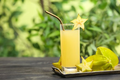 Photo of Delicious carambola juice and fresh fruits on wooden table against blurred background. Space for text