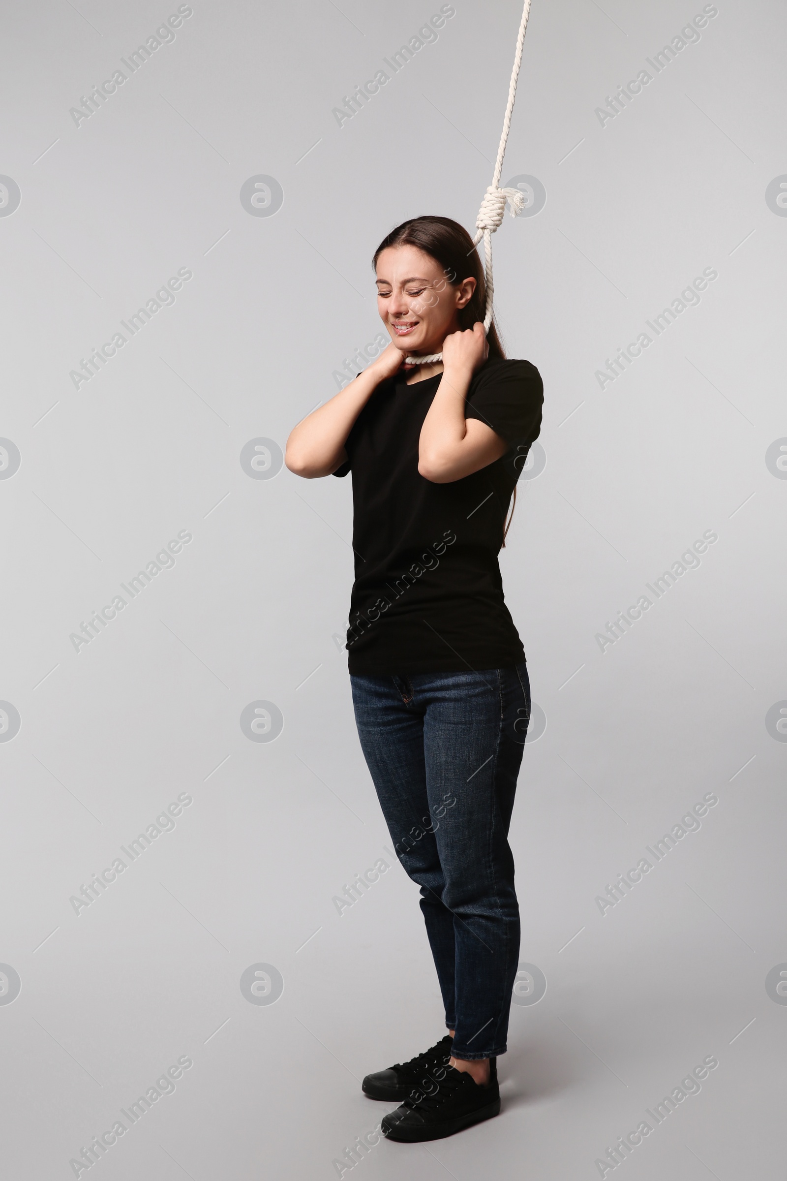 Photo of Depressed woman with rope noose on neck against light grey background