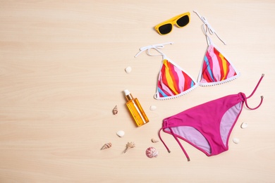 Photo of Beautiful bikini, sunglasses and bottle with sunscreen on wooden background, top view