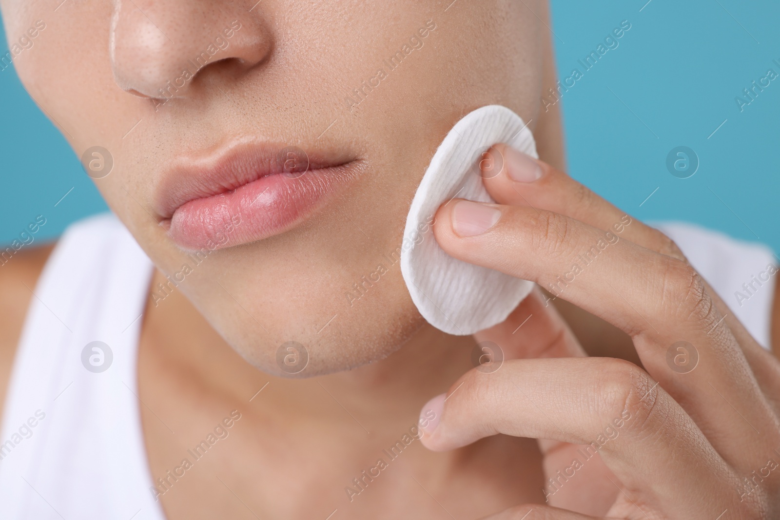 Photo of Man cleaning face with cotton pad on light blue background, closeup