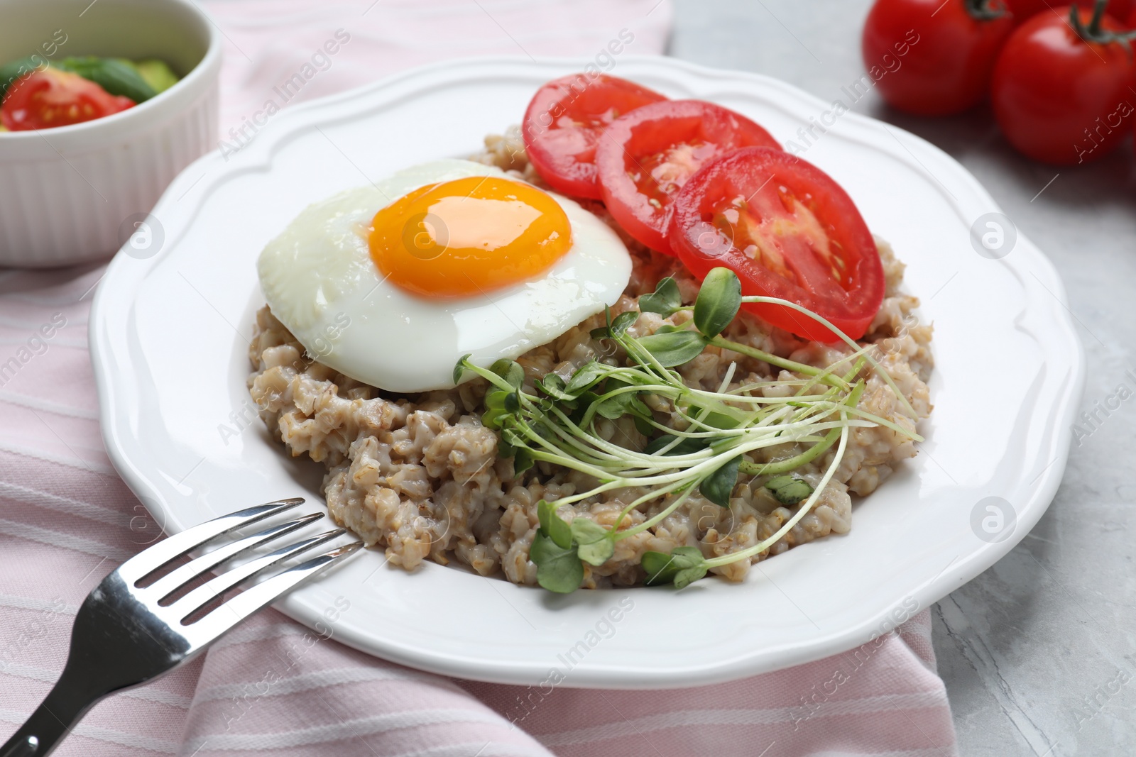 Photo of Delicious boiled oatmeal with fried egg, tomato and microgreens on table, closeup