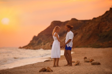 Photo of Young couple walking on beach at sunset