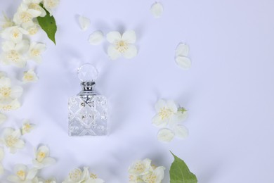 Aromatic perfume in bottle and beautiful jasmine flowers on white background, flat lay. Space for text