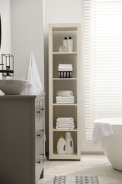Stylish bathroom interior with grey chest of drawers and shelving unit