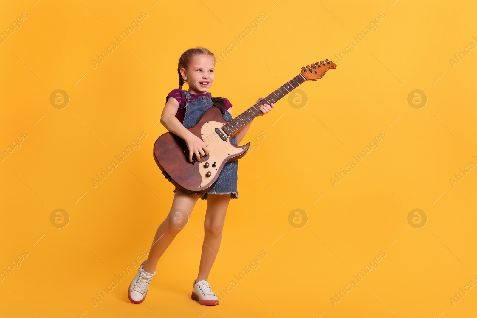 Photo of Cute girl with electric guitar on orange background