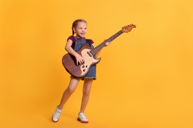 Cute girl with electric guitar on orange background