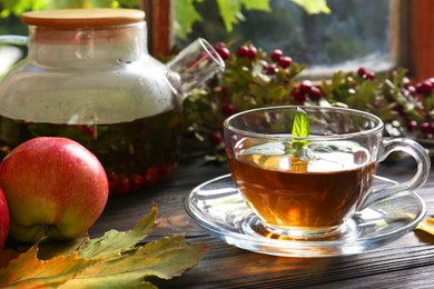 Photo of Hot tea, apples and dry leaves on wooden windowsill. Autumn atmosphere