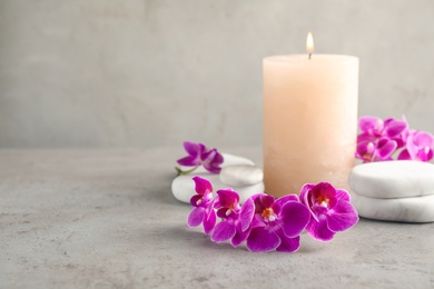 Photo of Orchid flowers, spa stones and candle on grey table. Space for text