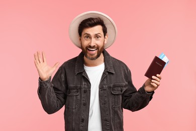 Smiling man with passport and tickets on pink background