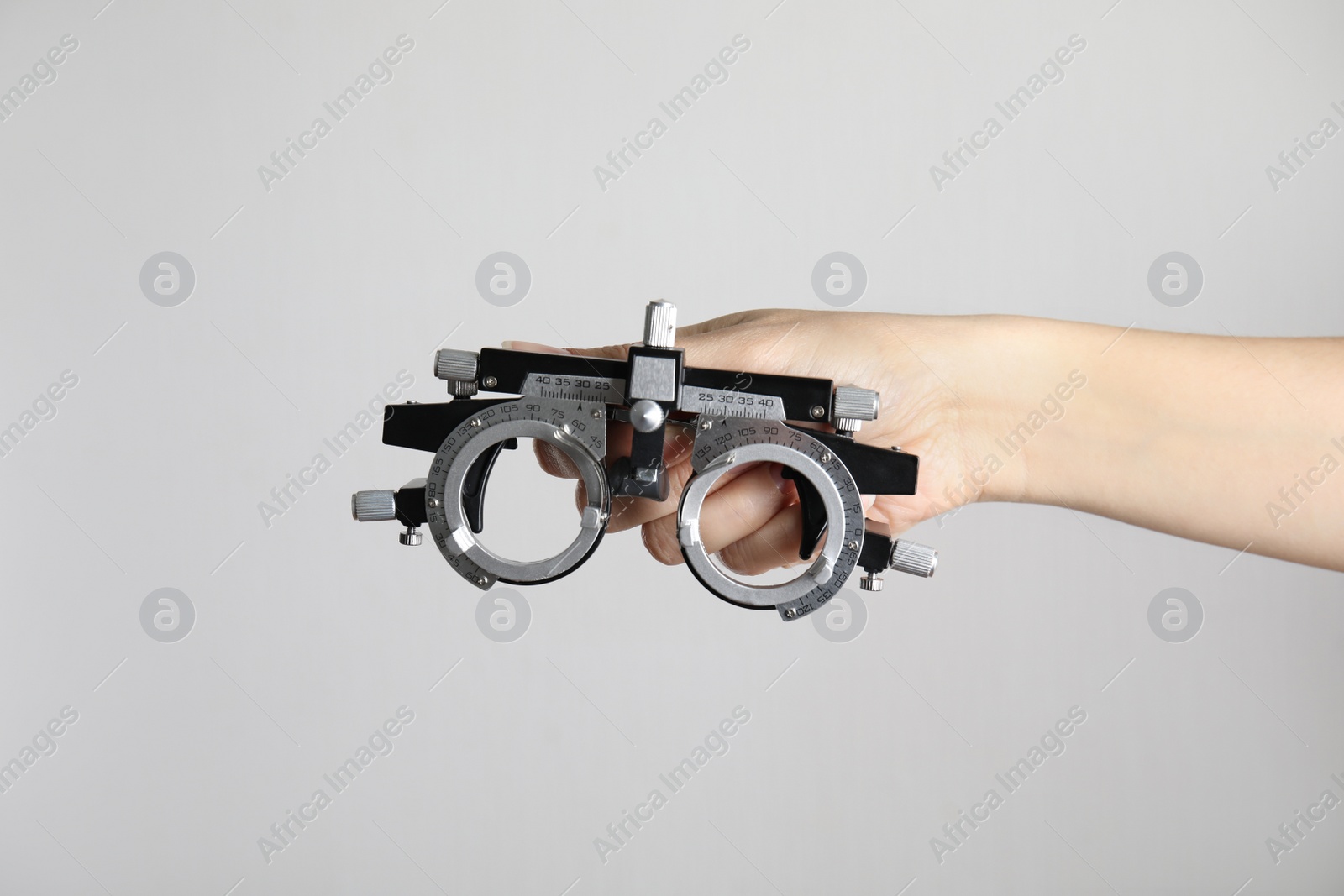 Photo of Woman holding trial frame on light background, closeup. Ophthalmologist tool