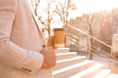 Photo of Businessman with cup of coffee on city street in morning, closeup