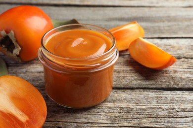 Delicious persimmon jam in glass jar and fresh fruits on wooden table, closeup