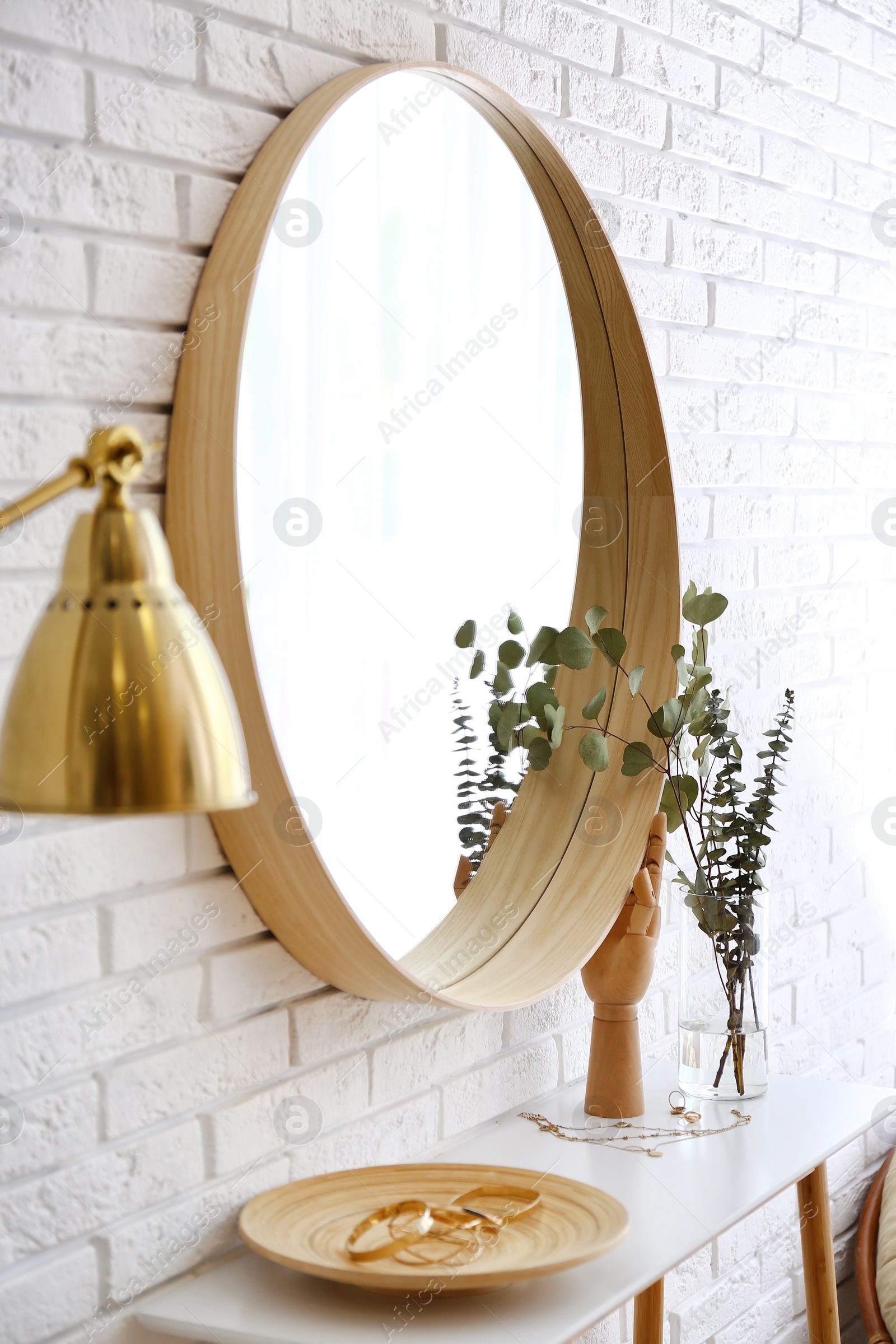 Photo of Big round mirror, table with jewelry and decor near brick wall in hallway interior