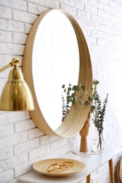 Photo of Big round mirror, table with jewelry and decor near brick wall in hallway interior