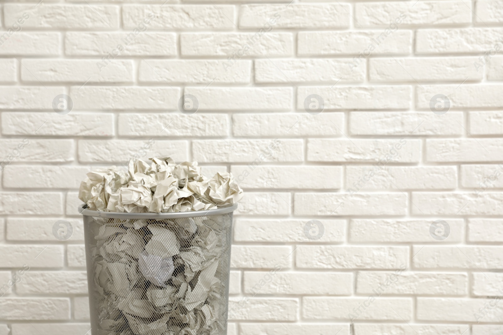 Photo of Metal bin with crumpled paper against brick wall, space for text