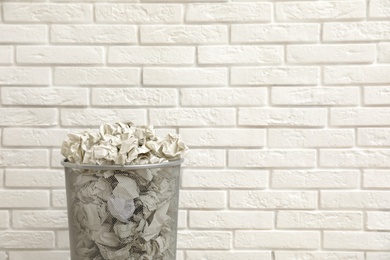 Photo of Metal bin with crumpled paper against brick wall, space for text