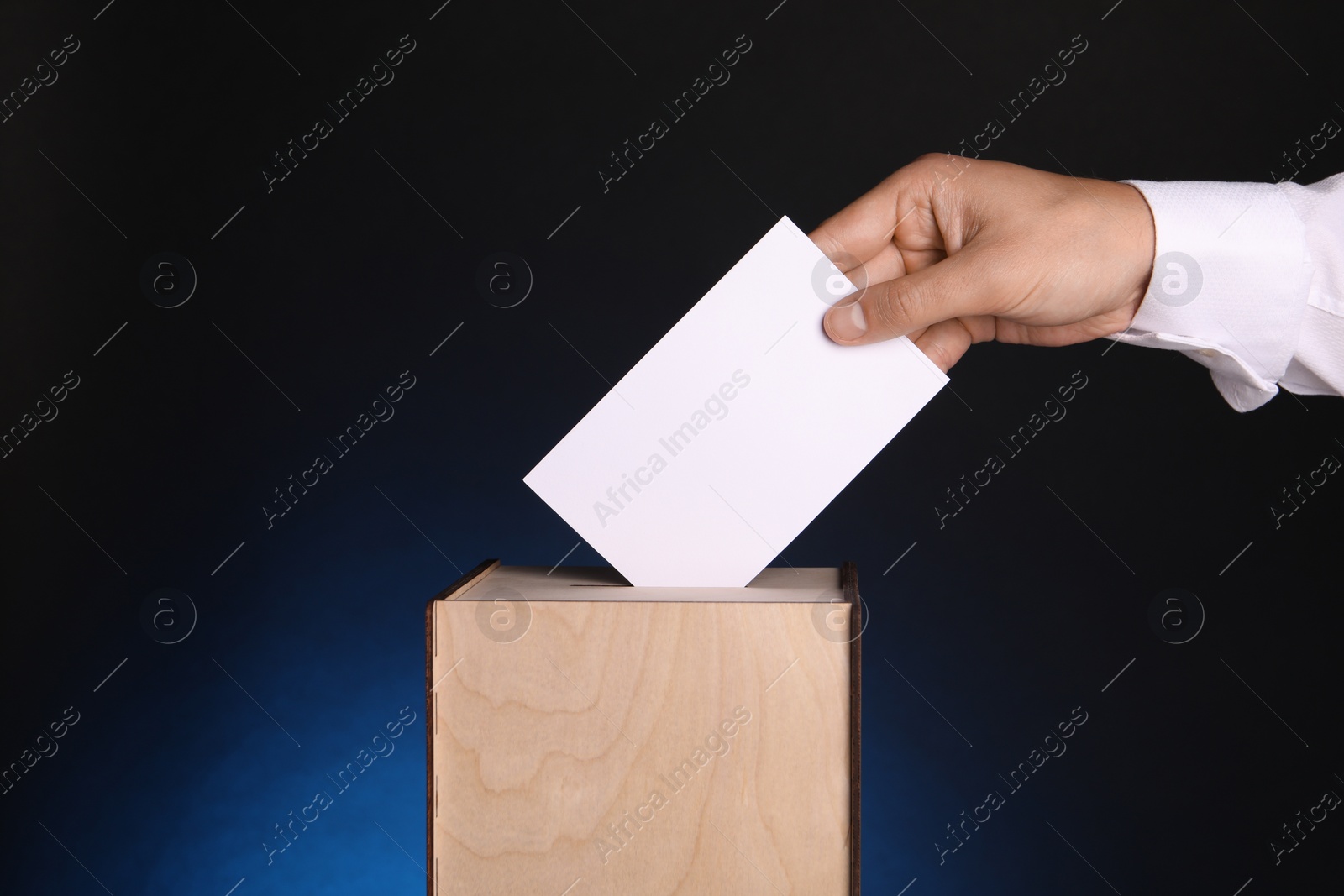 Photo of Man putting his vote into ballot box on dark blue background, closeup