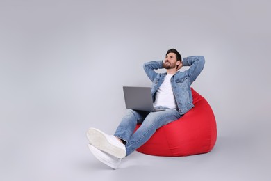 Happy man with laptop sitting on beanbag chair against light grey background