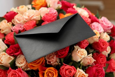 Photo of Black envelope on bouquet of beautiful roses, closeup