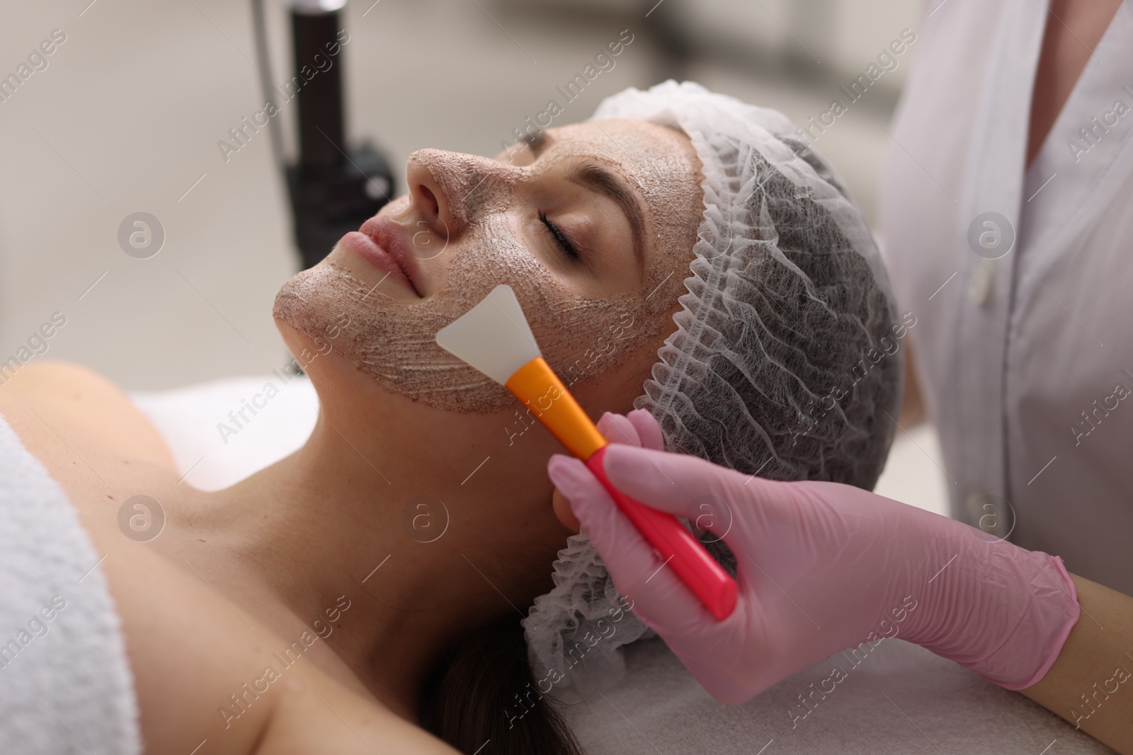 Photo of Cosmetologist applying mask on woman's face in clinic, closeup