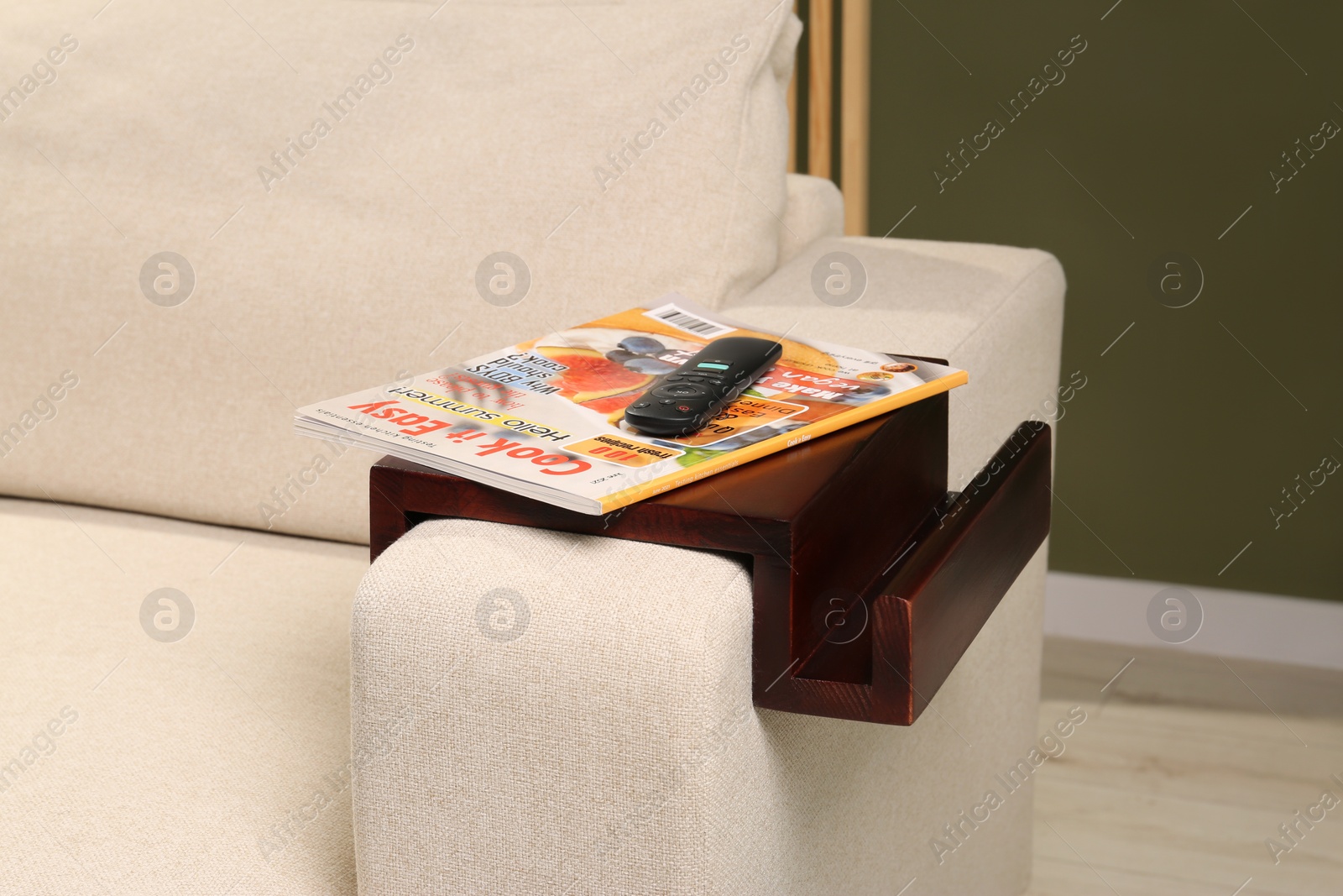 Photo of Magazine and remote control on sofa armrest wooden table in room. Interior element