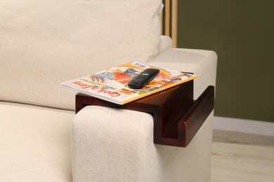 Magazine and remote control on sofa armrest wooden table in room. Interior element