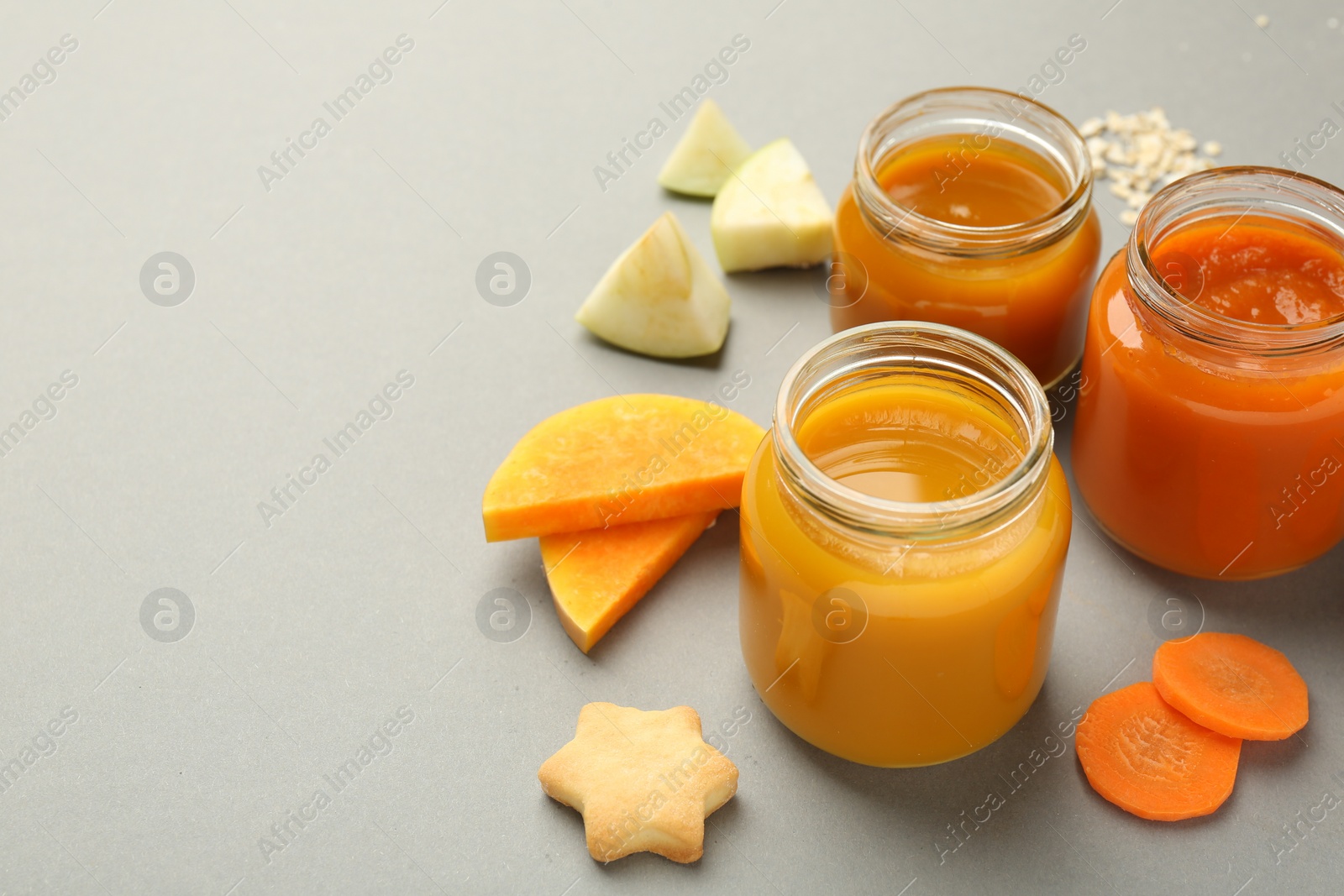 Photo of Jars with healthy baby food, vegetables, apple and cookie on grey background, space for text