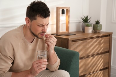 Photo of Man with glass of water taking pill at home. Suffering from terrible migraine