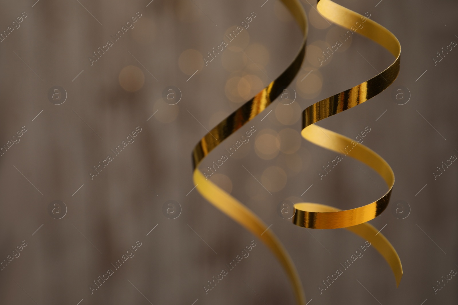 Photo of Shiny golden serpentine streamers against blurred lights, closeup. Space for text