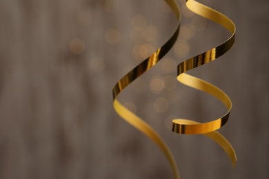 Shiny golden serpentine streamers against blurred lights, closeup. Space for text