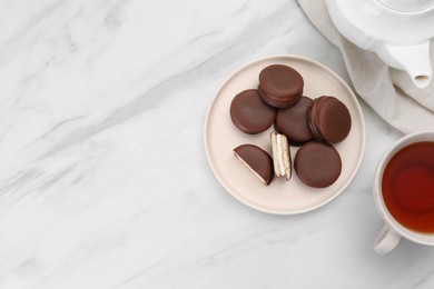 Photo of Plate with delicious choco pies and cup of tea on white marble table, flat lay. space for text