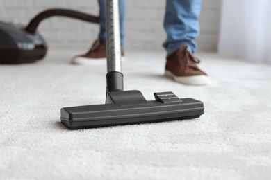 Man cleaning carpet with vacuum at home