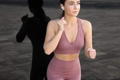 Young woman in stylish sports wear running near dark mirror wall