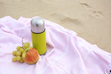 Metallic thermos with hot drink, fruits and plaid on sandy beach, space for text